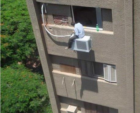 Man sat on an aircon unit on side of a building 