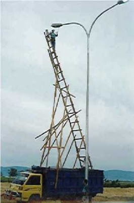 man balanced on a very tall ladder changing a light bulb