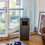 Airconco Arctic portable air conditioner in a living room, white and dark brown case, hose going out balcony door