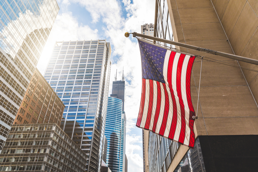 Amercian flag below amercian glass skyscrapers